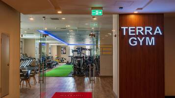 En entré till ett gym med en skylt som visar texten ”TERRA GYM”, träningsutrustning, en grön matta och en röd välkomstmatta.