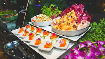 A buffet with various dishes including salads, a bowl of mango chunks, and small plates with salmon garnished with flowers.