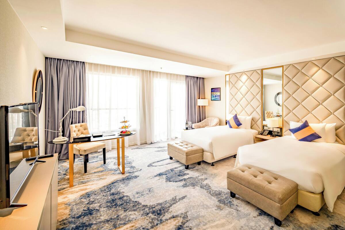 Habitación de hotel con dos camas, un escritorio, una silla, un televisor y un espejo grande.