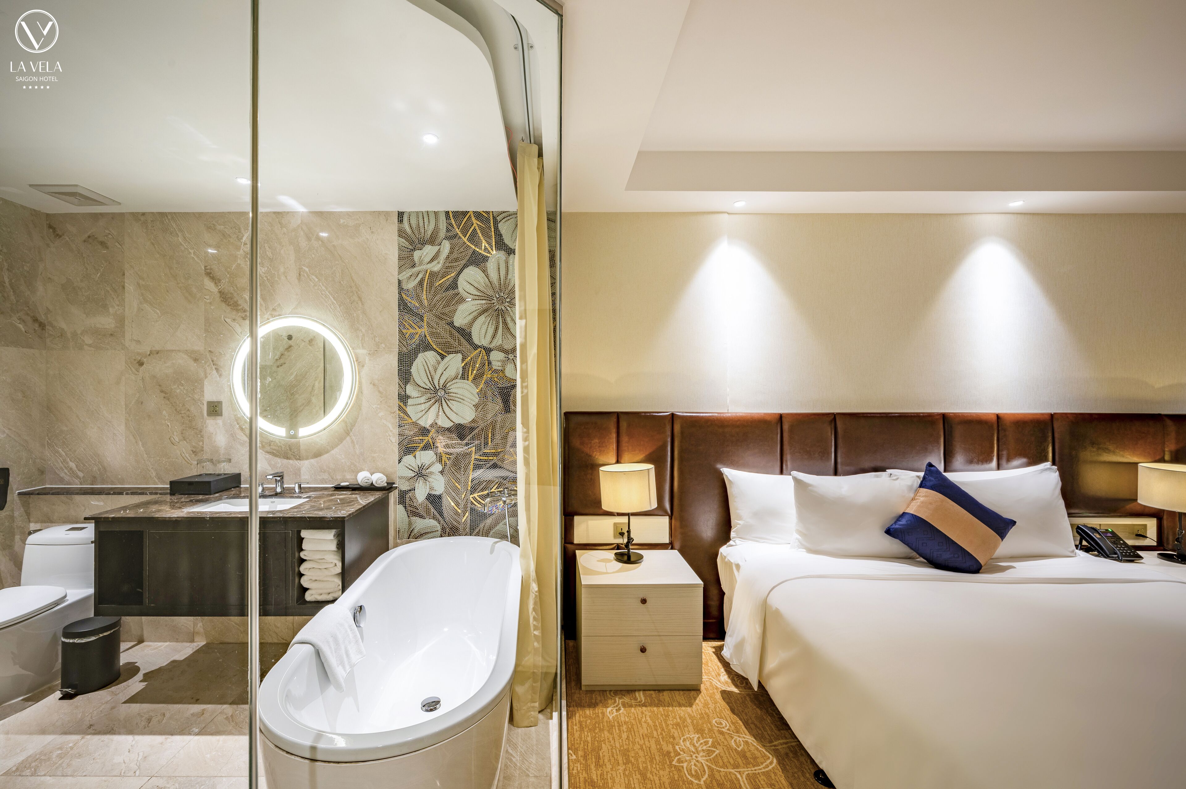 A modern hotel room with a marble bathroom, a large bed with a headboard, and a bedside table with a lamp.