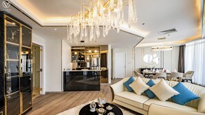 Un interior de hotel moderno con un comedor, una sala de estar con sofá y mesa de centro, y una cocina visible a través de un umbral abierto.
