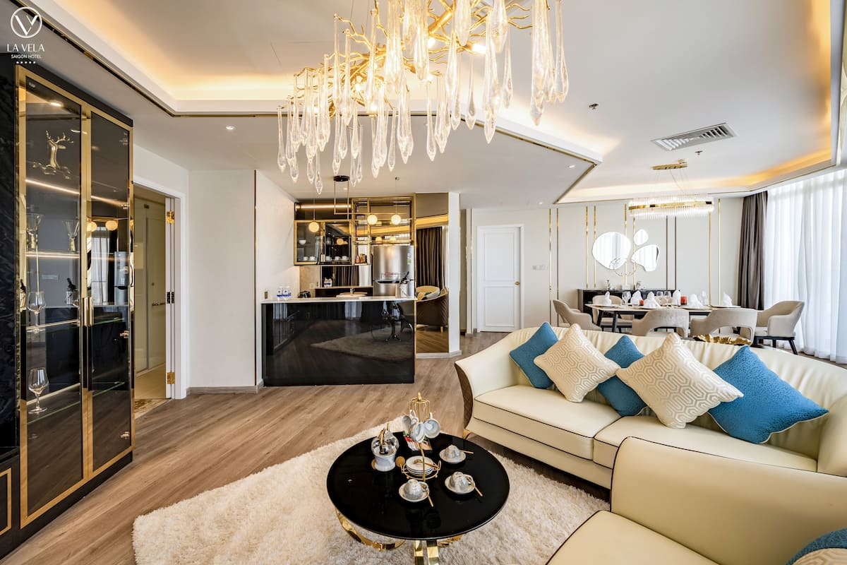 Un interior de hotel moderno con un comedor, una sala de estar con sofá y mesa de centro, y una cocina visible a través de un umbral abierto.