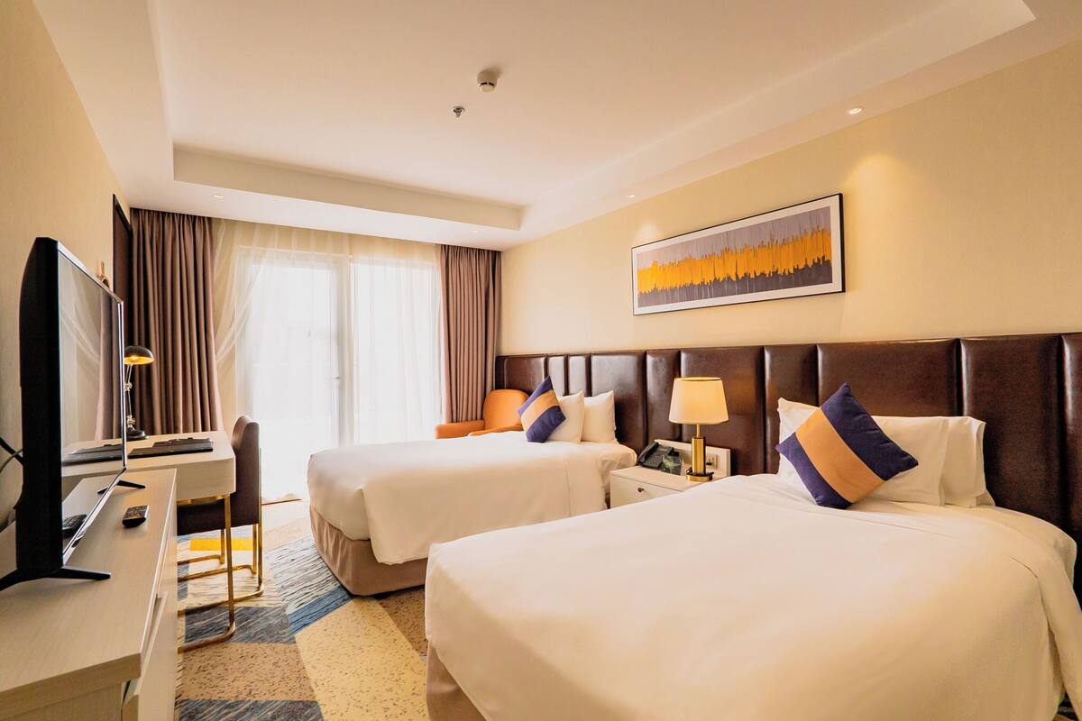 Habitación de hotel con dos camas, un escritorio, un televisor y una ventana con cortinas.