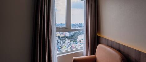 A room with a large window, a view of a cityscape, and a brown leather chair.