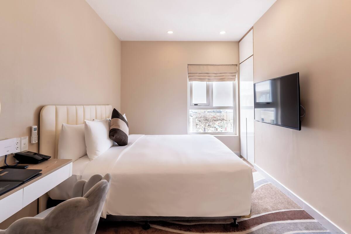 Una habitación de hotel con una cama, un escritorio con una silla, un televisor montado en la pared y una ventana con vistas a la ciudad.