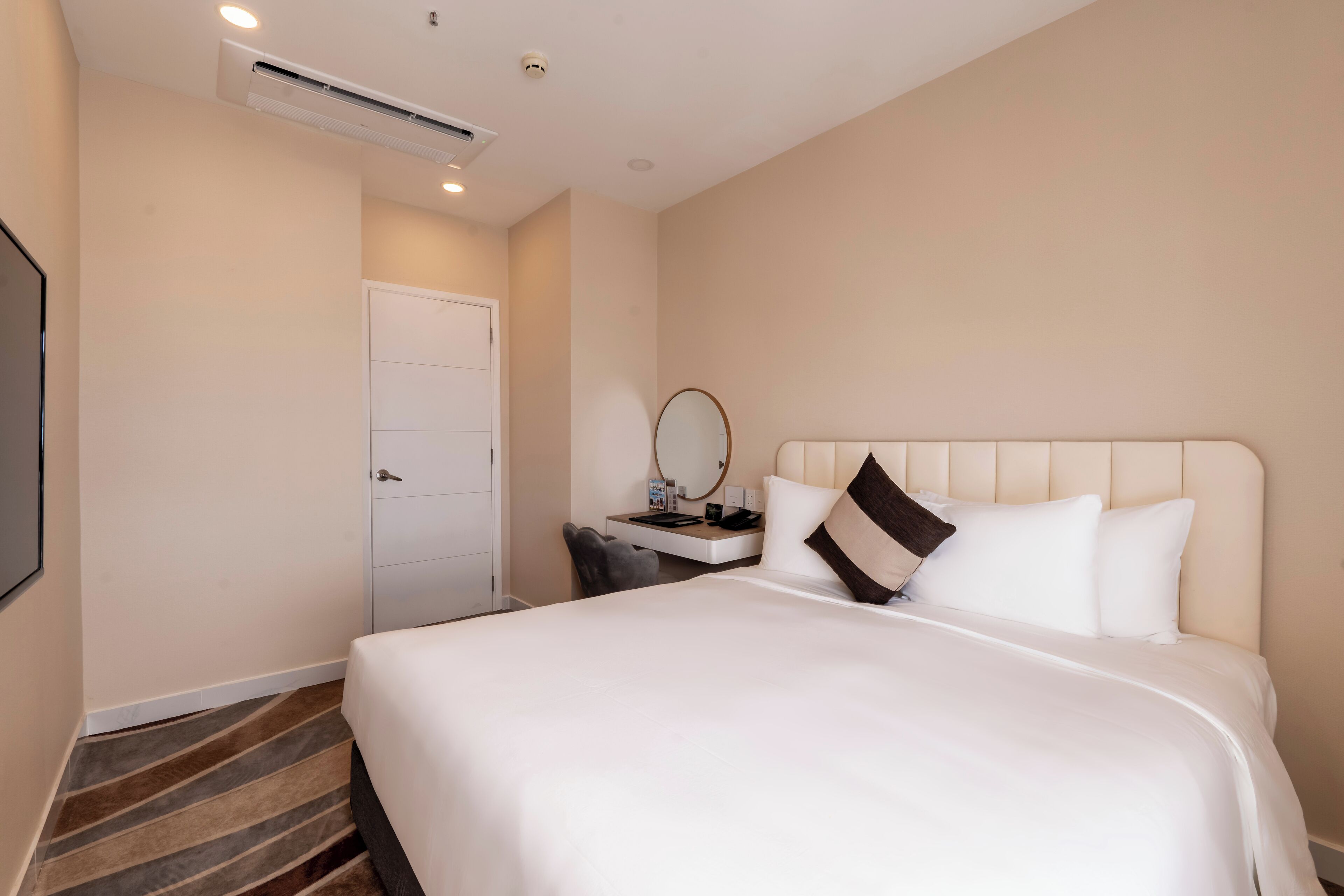 Habitación de hotel con una cama grande, una mesita de noche con lámpara, un espejo y una puerta.