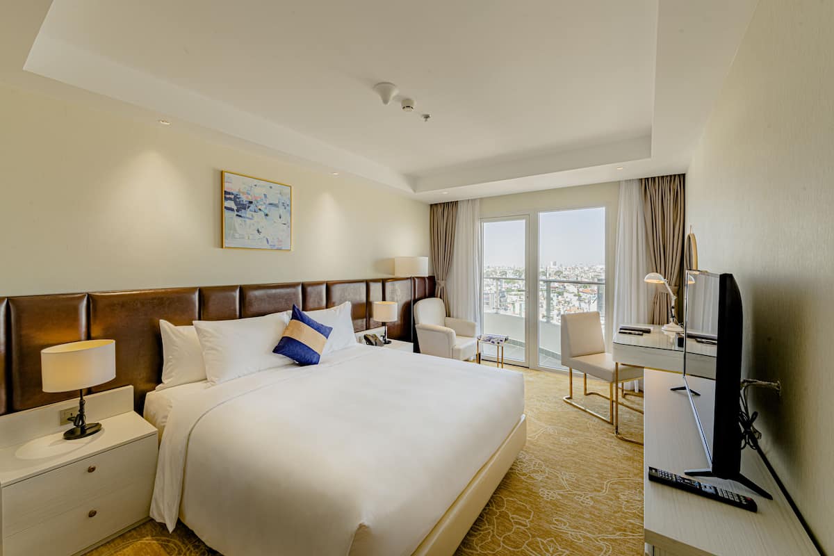 Habitación de hotel con una cama grande, un escritorio con computadora, un televisor y vistas a la ciudad por la ventana.