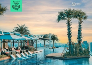 Zona de piscina con sillas de descanso, un espacio de estar cubierto y palmeras.