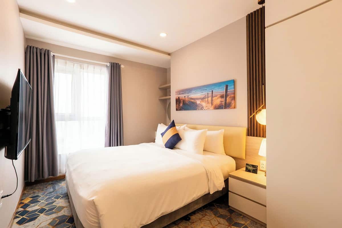 Habitación de hotel con una cama grande, un televisor de pantalla plana, una mesita de noche con lámpara y un cuadro en la pared.