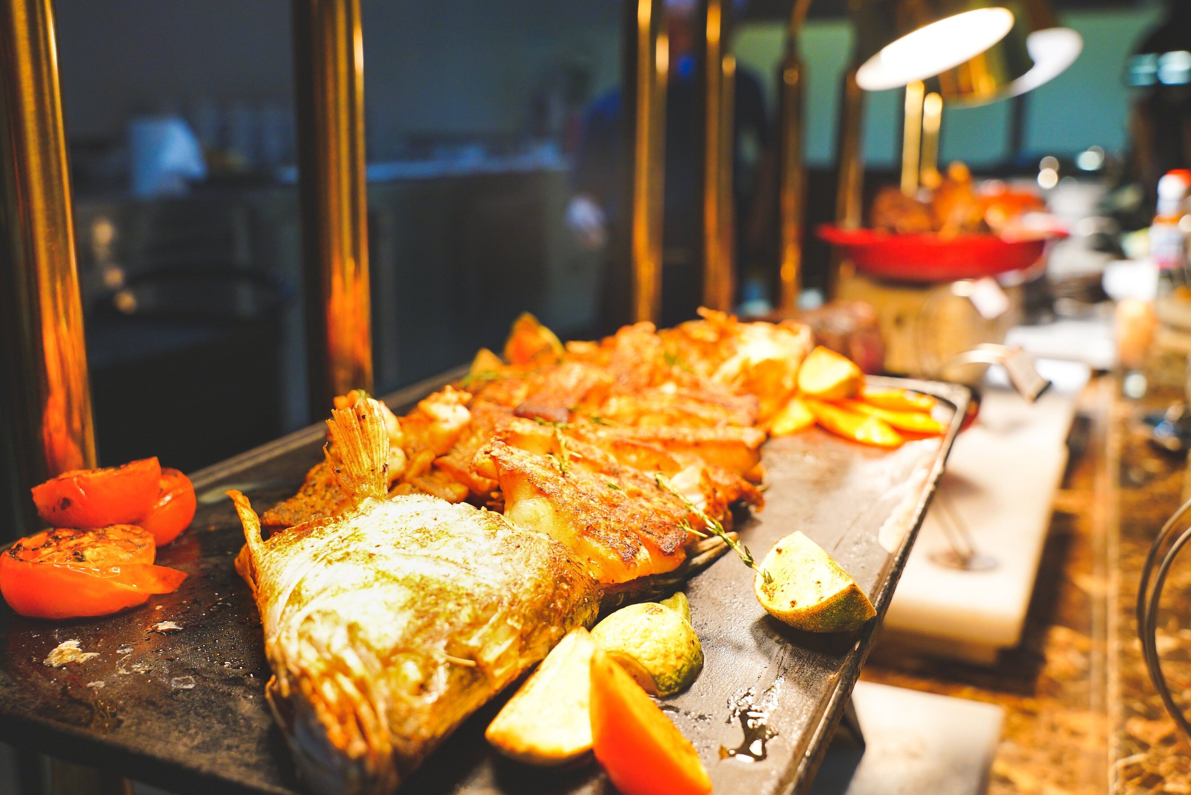 A buffet table with various dishes, including roasted fish and vegetables.
