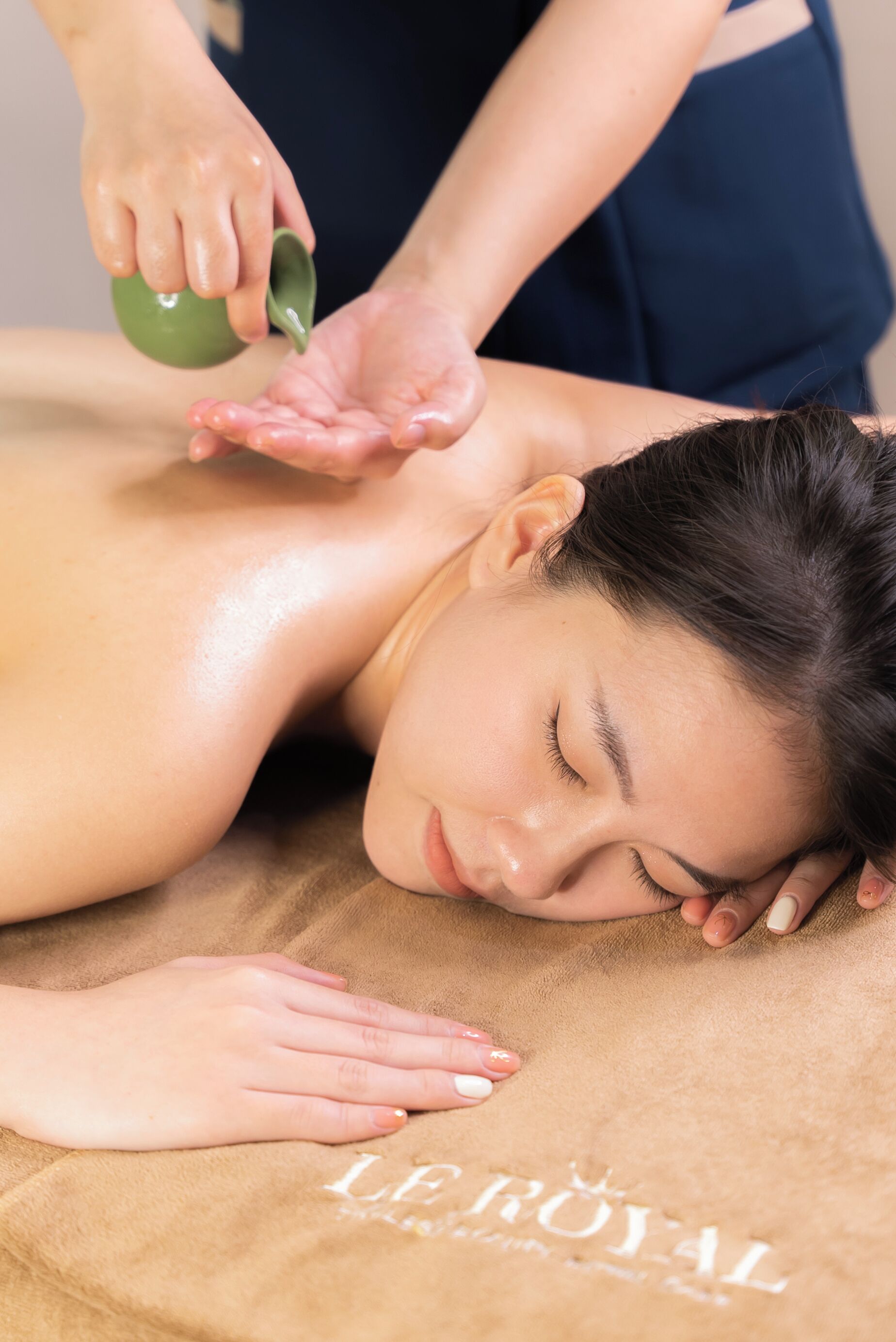 A person receiving a massage with a towel labeled 'LE ROYAL' on the floor.