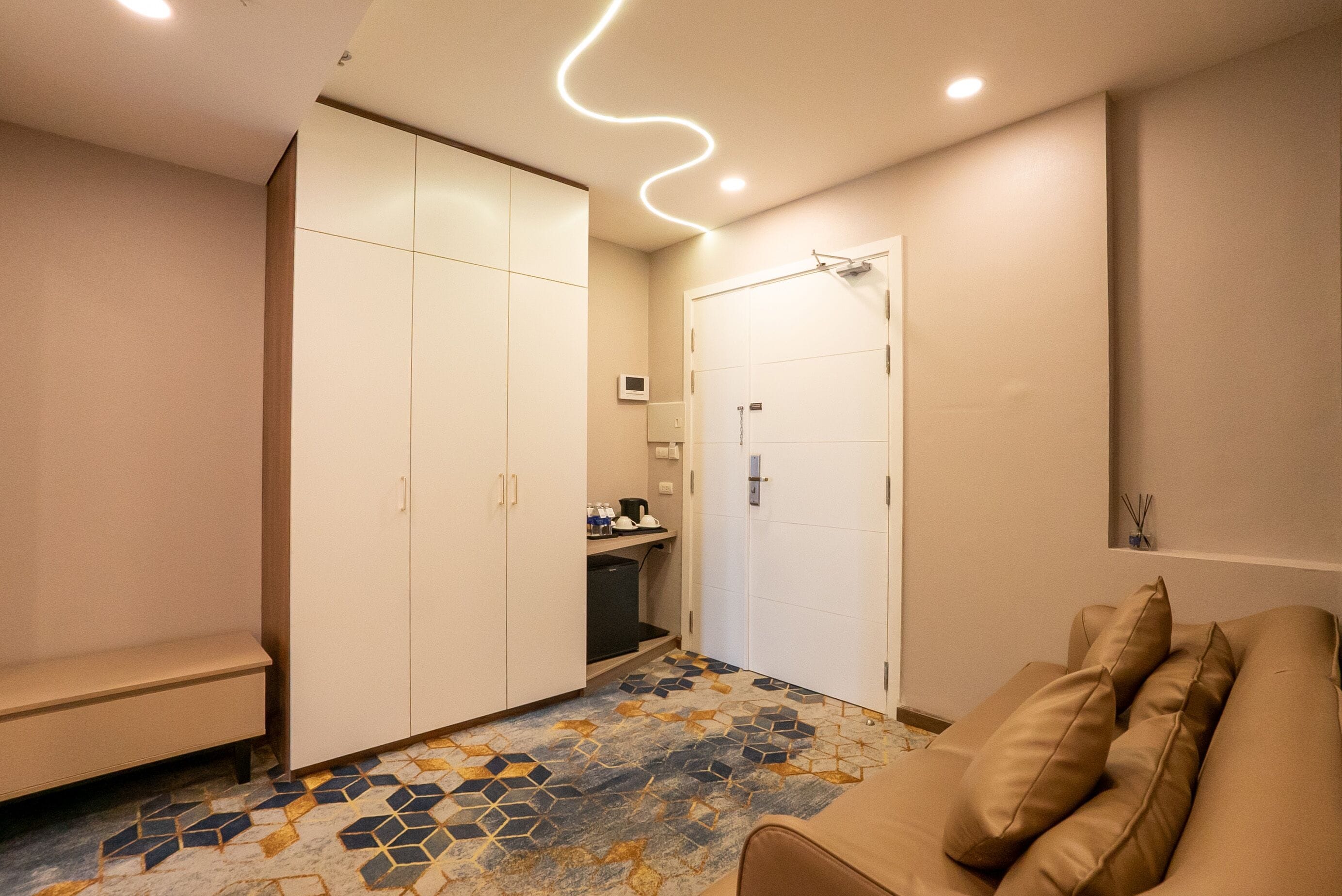 A hotel room with a sofa, a bench, a wardrobe, a shower, and a tiled floor.