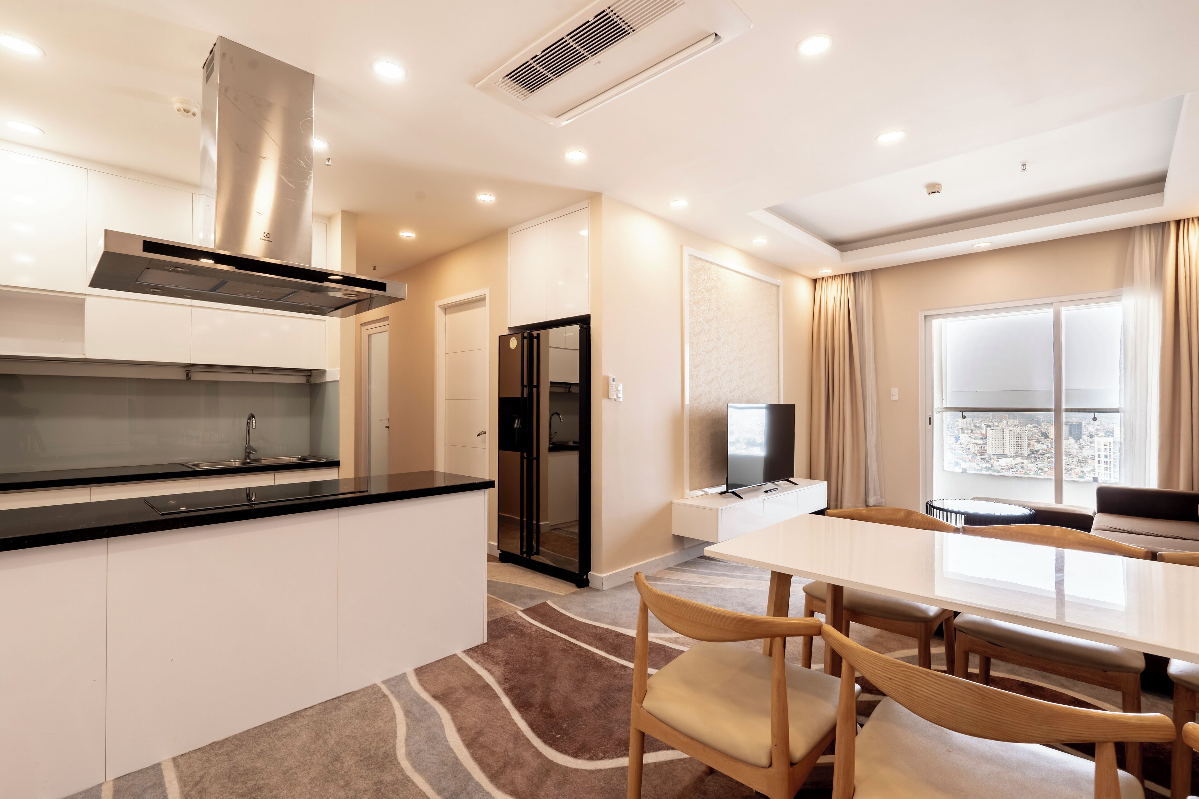 Una cocina moderna con una campana extractora de acero inoxidable, un comedor con una mesa grande y sillas, y vistas de la ciudad a través de un ventanal.