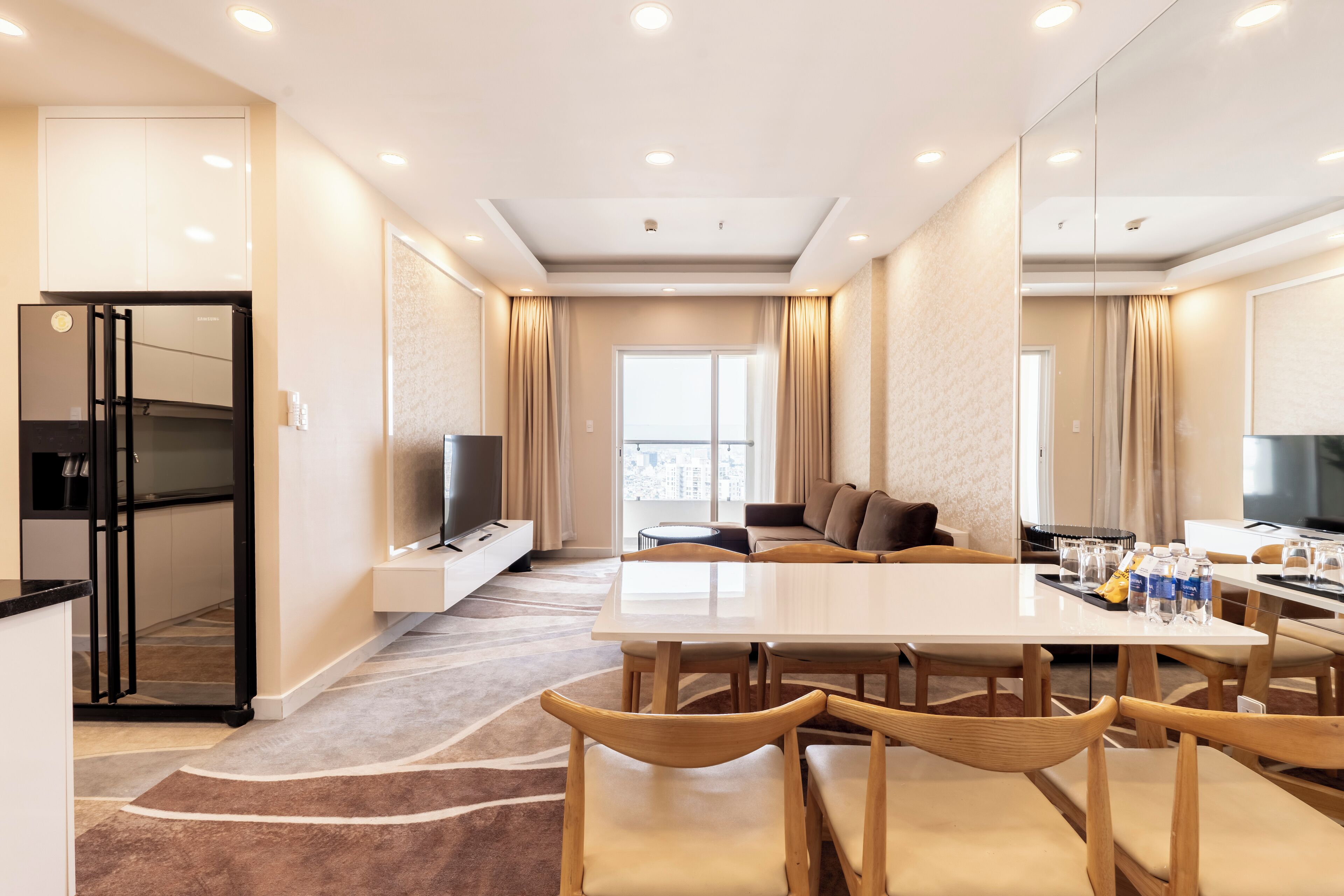 A modern hotel room with a dining area, a sofa, a TV, and a kitchen area.