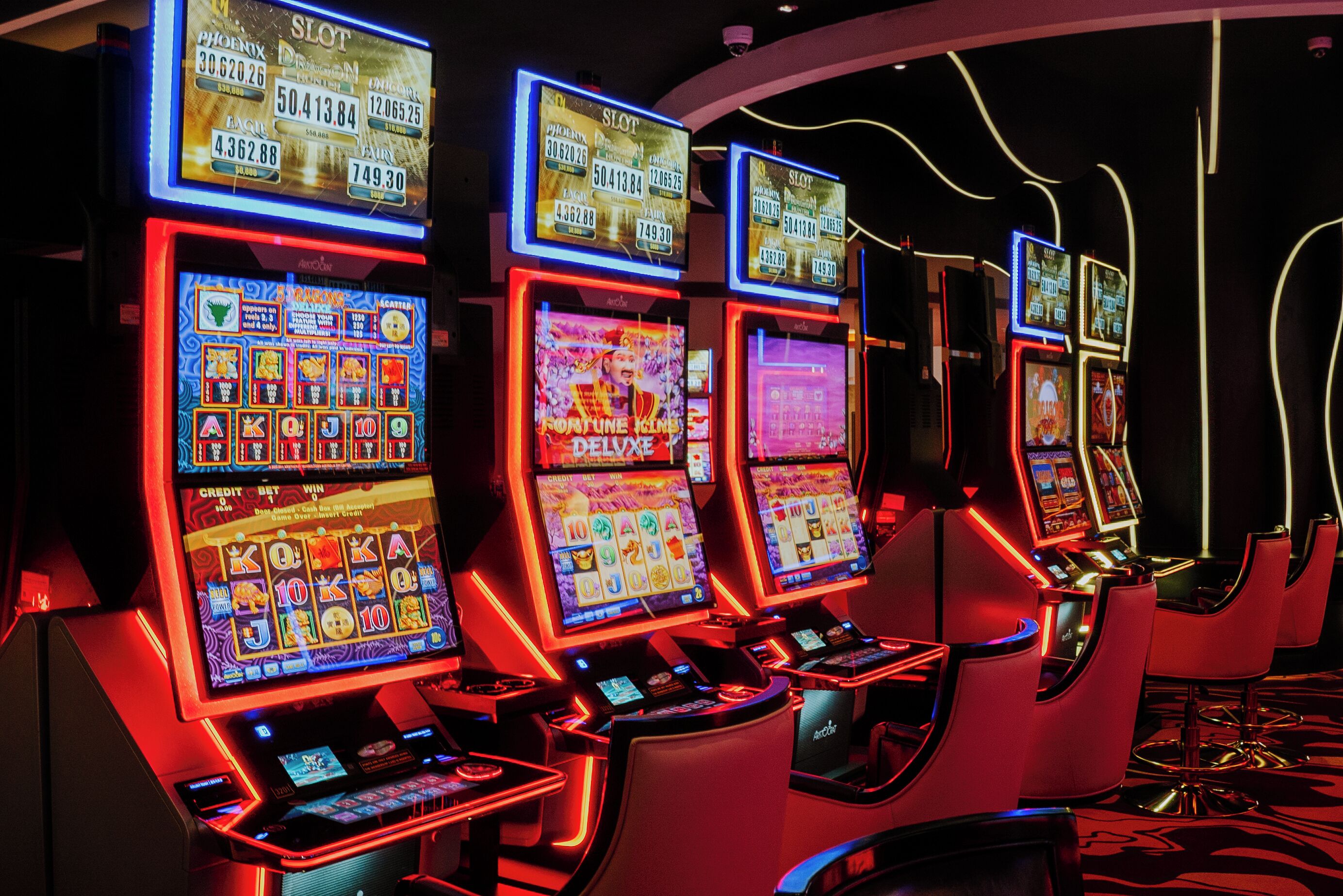 A row of slot machines in a casino with illuminated screens and red lighting.