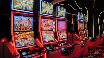 A row of slot machines in a casino with illuminated screens and red lighting.