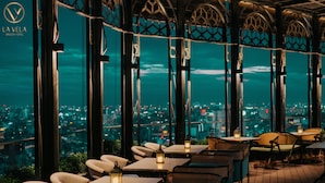 Un restaurante con mesas y sillas, ventanas amplias y vista a la ciudad de noche.