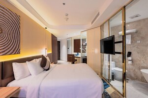 A modern hotel room with a large bed, a desk, a TV, and a bathroom with a glass partition.