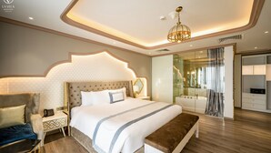 Una habitación de hotel moderna con una cama grande, mesitas de noche, un banco, un sofá, un baño con bañera y un vestidor.