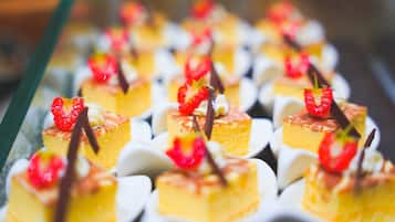 A tray of small yellow desserts topped with strawberries and chocolate, arranged on white plates.