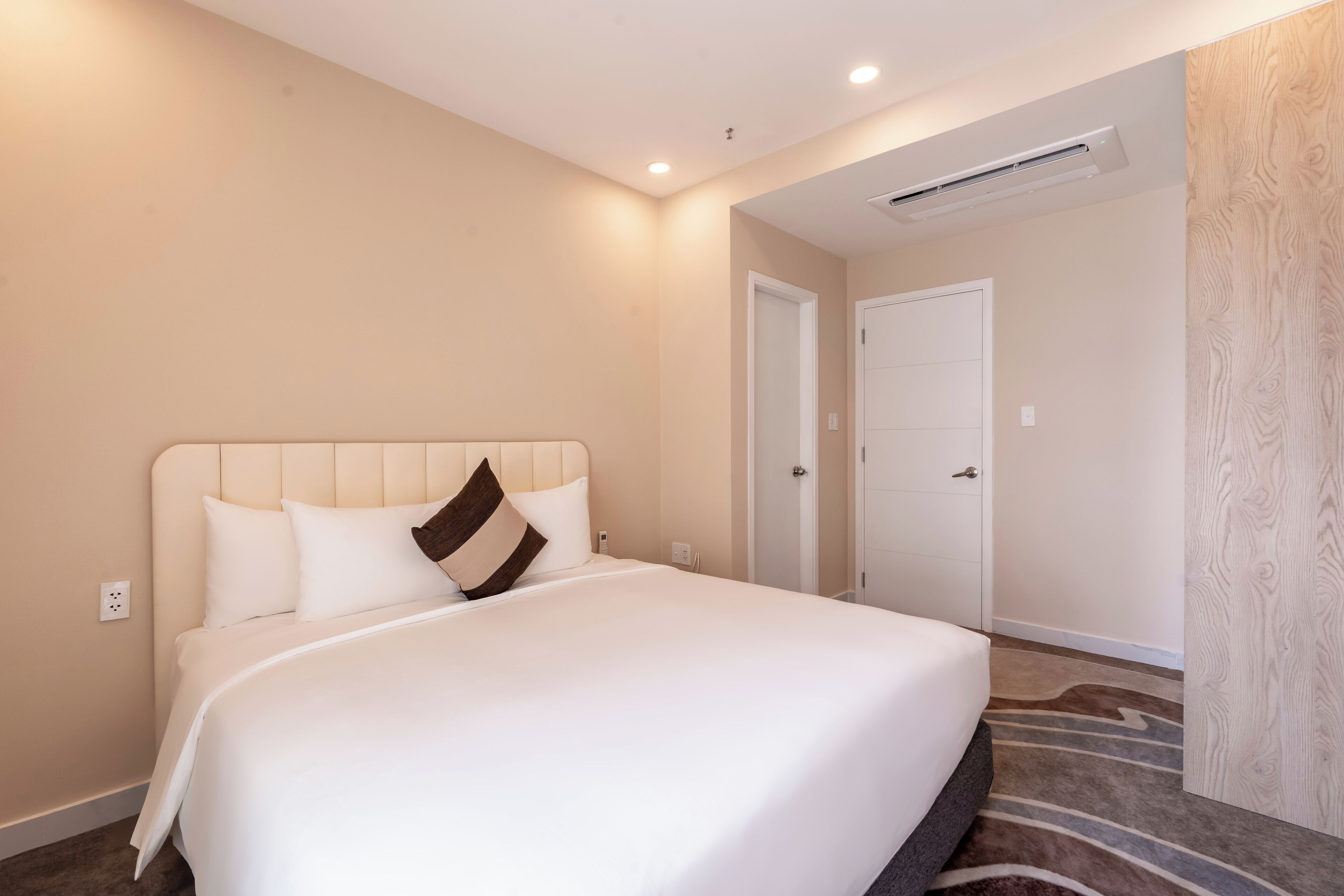 A hotel room with a large bed, a door, and an air conditioning unit on the wall.