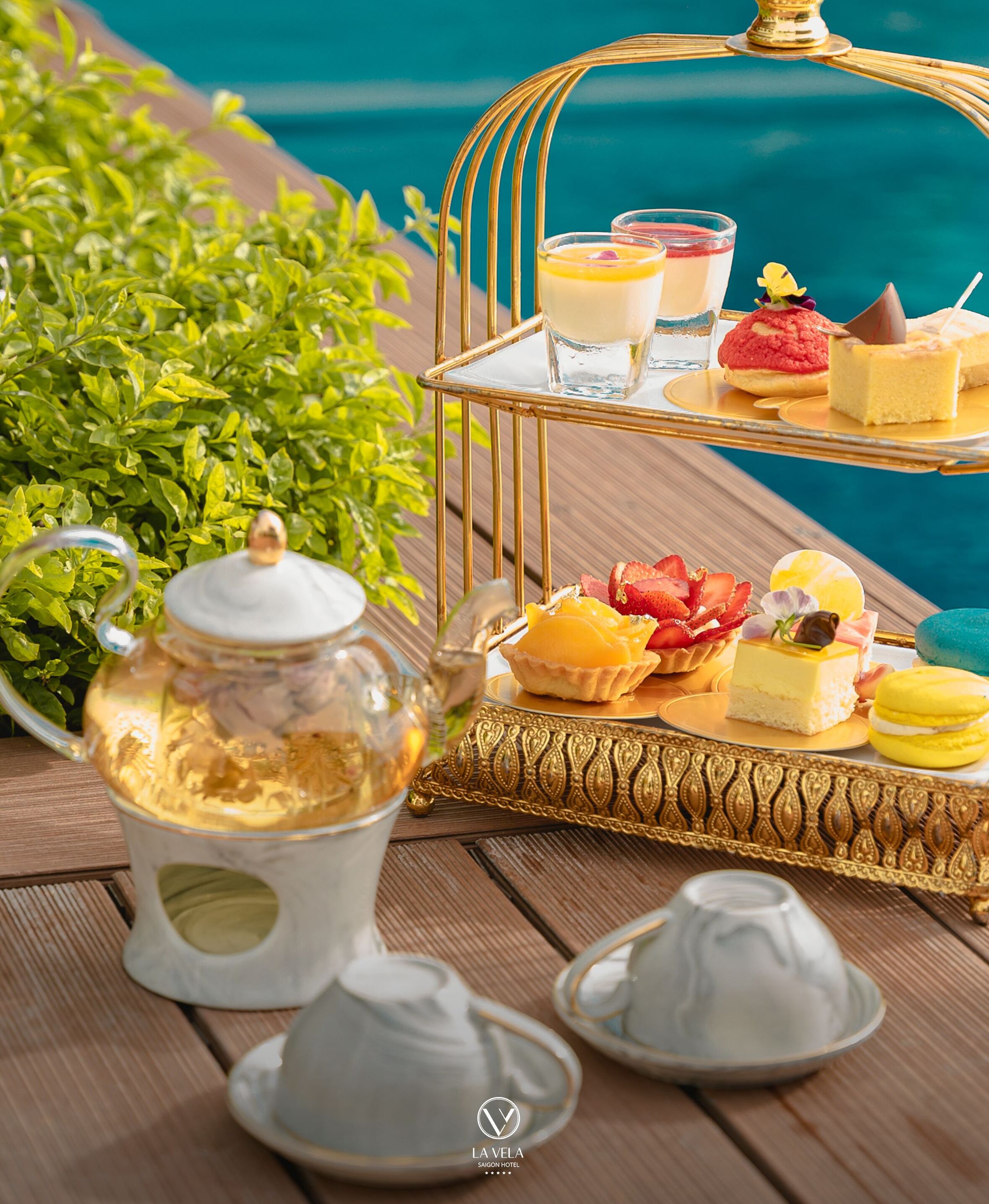 A table with a tea set, a tray of desserts, and a view of the sea.