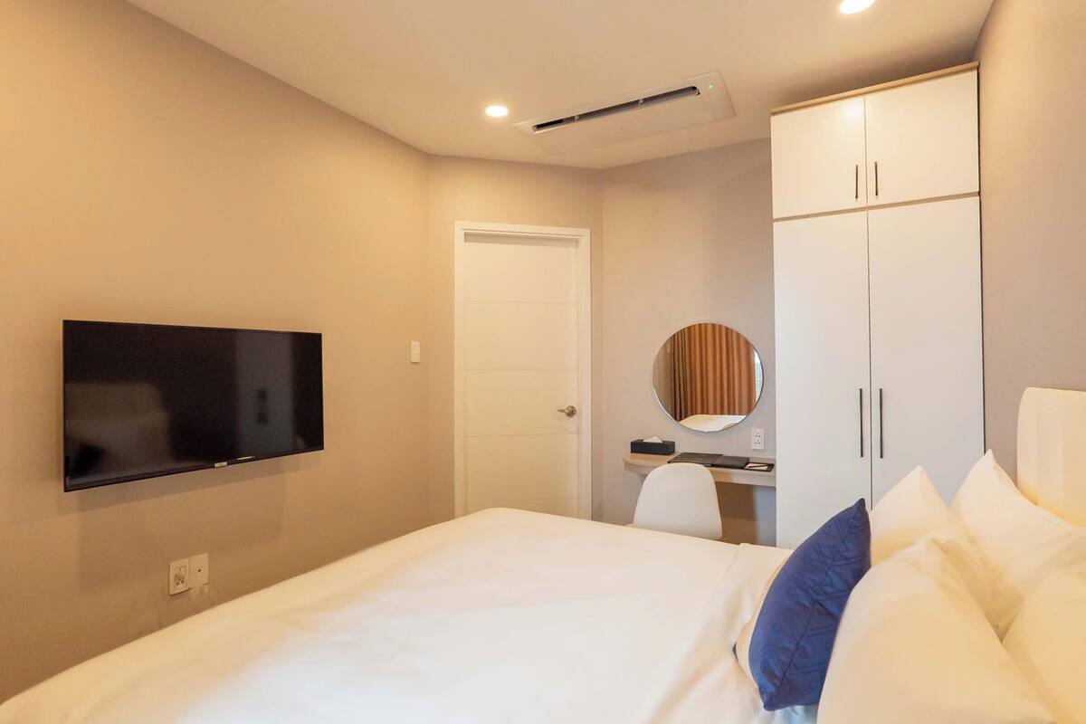 Una habitación de hotel con una cama, un televisor montado en la pared, un armario y un escritorio con una silla.