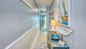 A hallway with a coat rack, a welcome sign, a lamp, a bowl, and a painting on the wall. - Beachfront, Indoor Pool & Hot Tub (Gulf Shores)