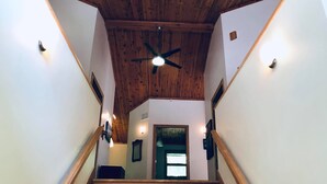 Una escalera de madera con ventilador de techo, paredes blancas y una puerta en la parte superior.