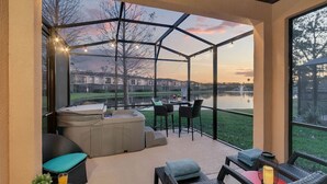 A covered patio with a hot tub, seating area, and a view of a lake and buildings. - 5708 Lakefront Retreat w/ Pool/Jacuzzi Near Disney (Kissimmee)