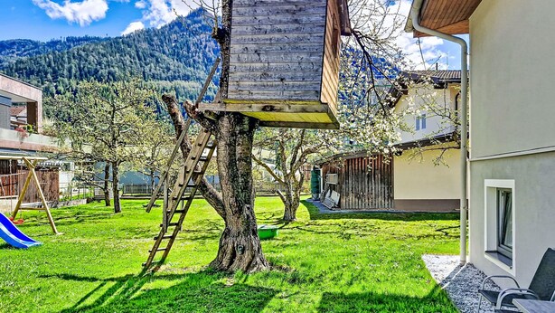 Una casa en el árbol sujeta a un árbol, un tobogán y un edificio con una ventana.