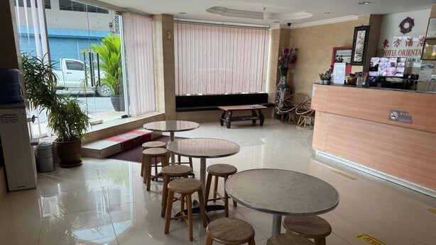 A hotel lobby with round tables and stools, a reception desk, and a large window with blinds. - Hotel O Hotel Oriental (Kota Kinabalu)