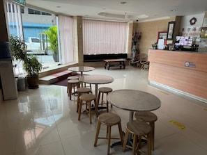 A hotel lobby with round tables and stools, a reception desk, and a large window with blinds.