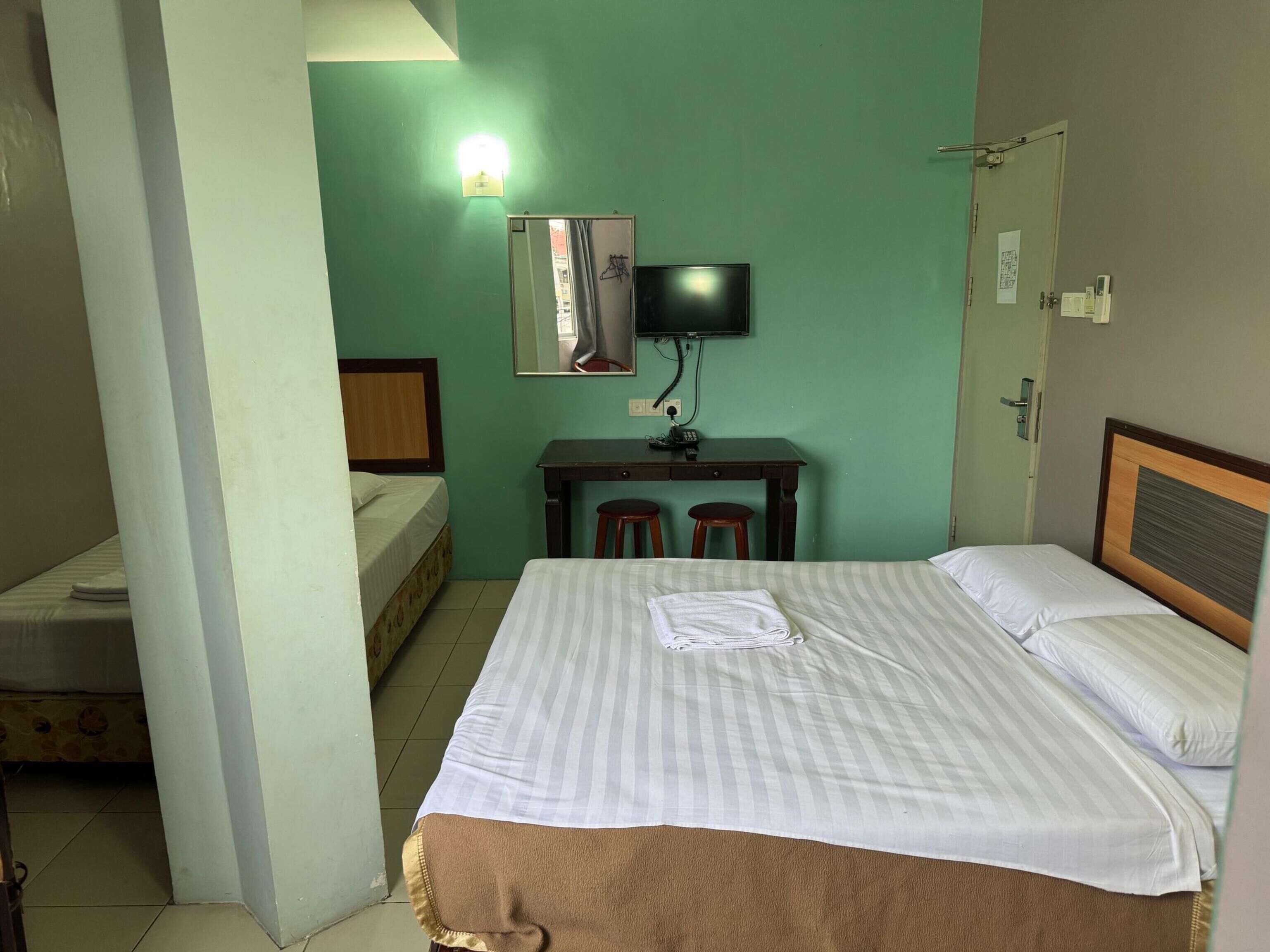 Una habitación de hotel con cama, escritorio, silla, televisor y espejo.