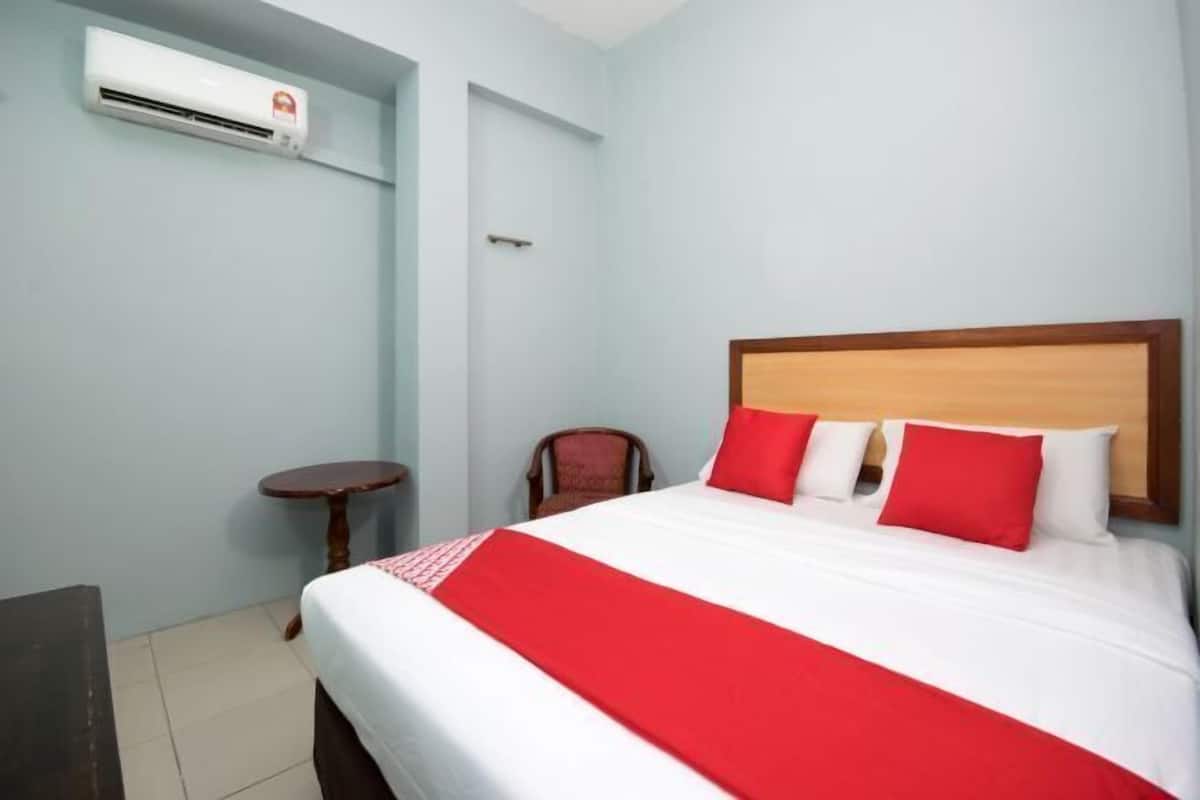 A hotel room with a bed, a small round table, a chair, and an air conditioning unit.