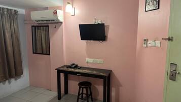 Une petite pièce comprenant un bureau, une chaise, un appareil de climatisation, un téléviseur et une porte avec une serrure.