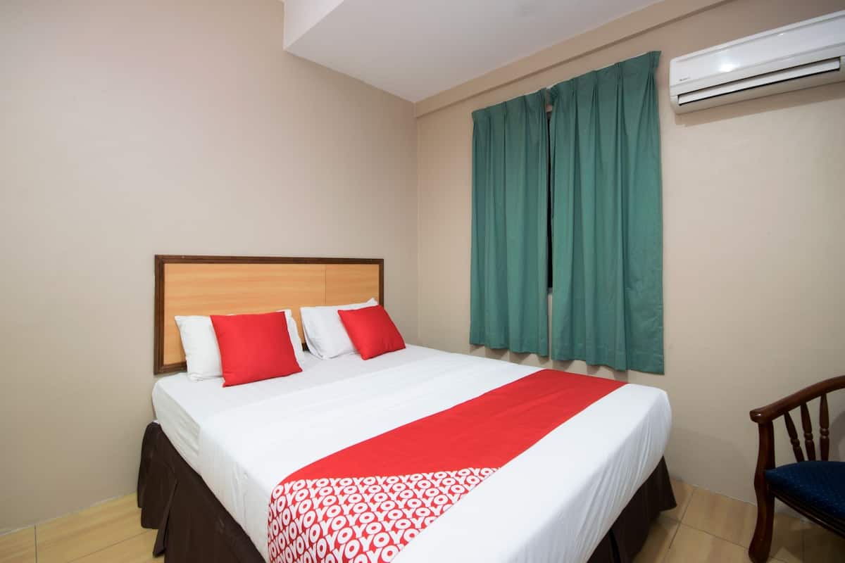 A hotel room with a bed, a chair, and an air conditioning unit on the wall.