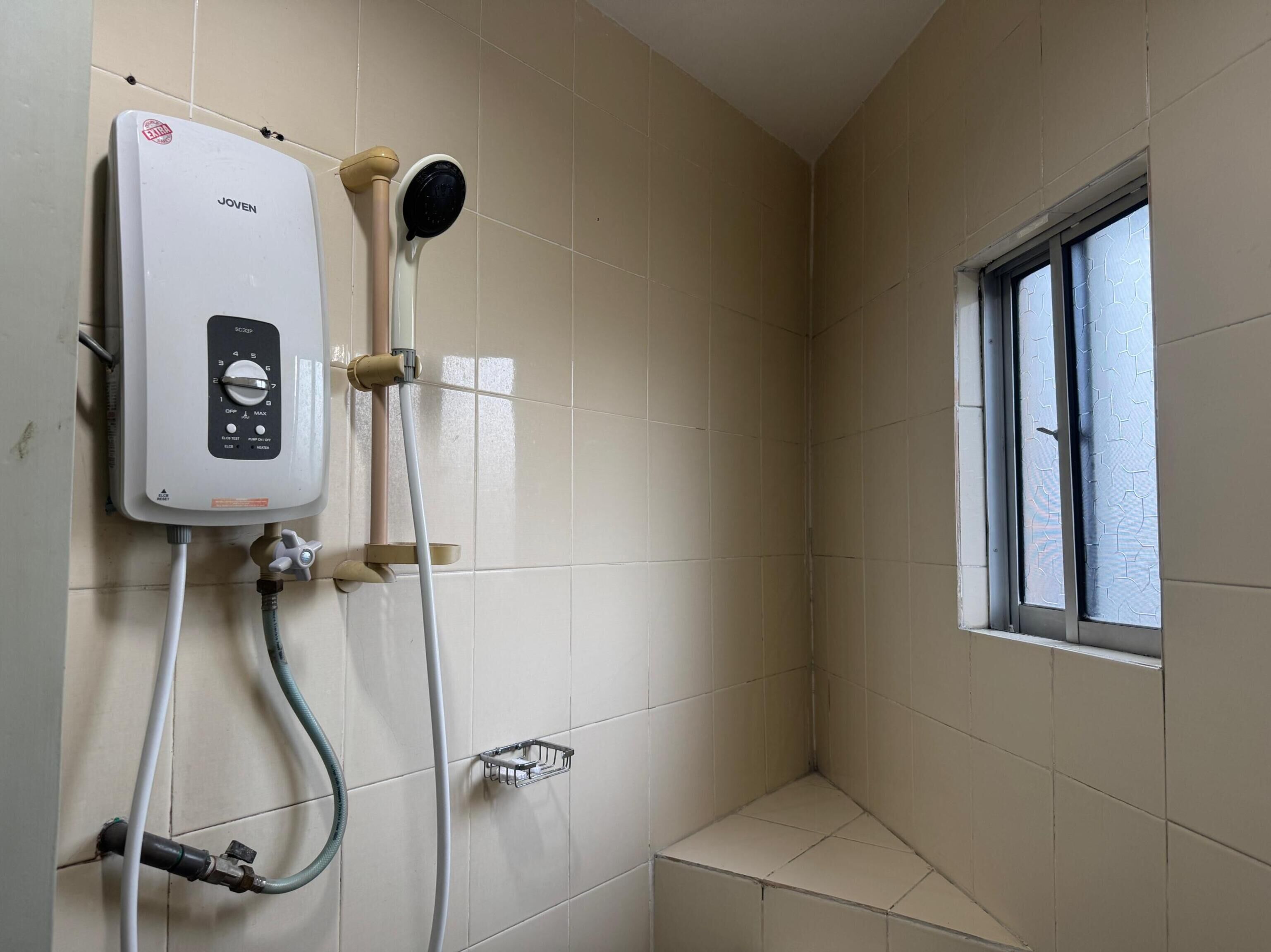 A shower area with a Joven water heater, a handheld showerhead, and a window.