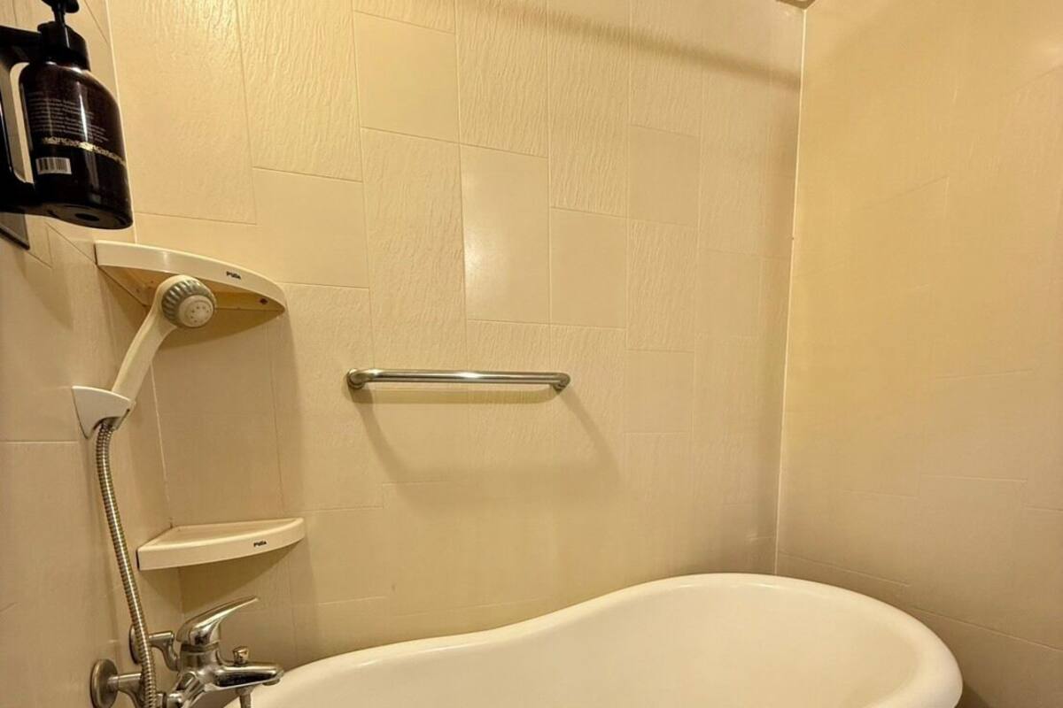A bathroom with a white bathtub, a handheld showerhead, a soap dispenser, and a towel rack.