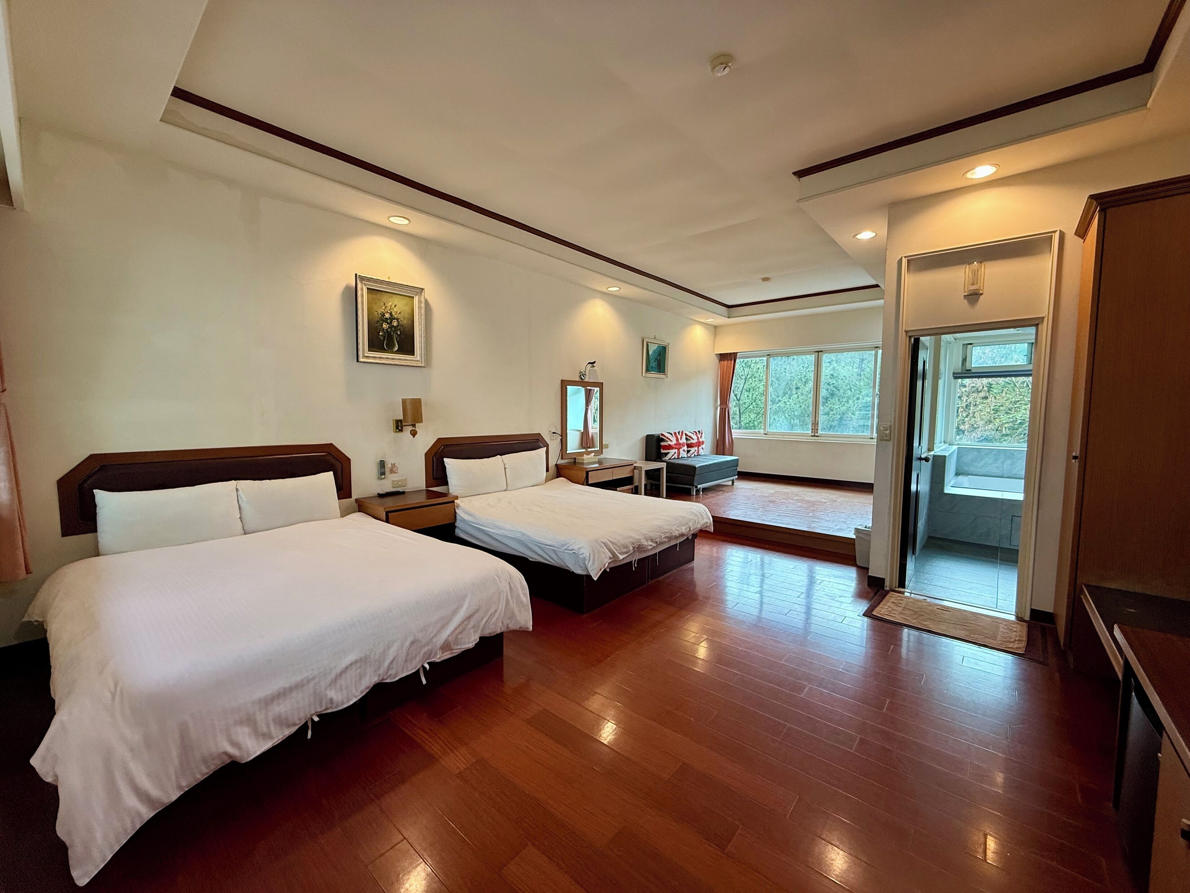 Habitación de hotel con dos camas, un escritorio, una silla, una ventana y una puerta que da a un balcón.