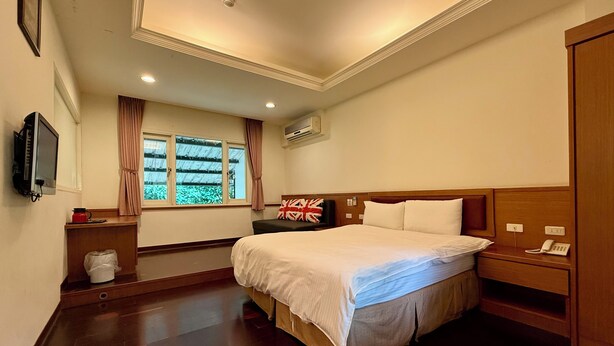A hotel room with a large bed, a bedside table with a phone, a small desk with a computer, a window with curtains, and a wall-mounted TV. - Mei Zhi Lin Holiday Homestay (Guoxing)