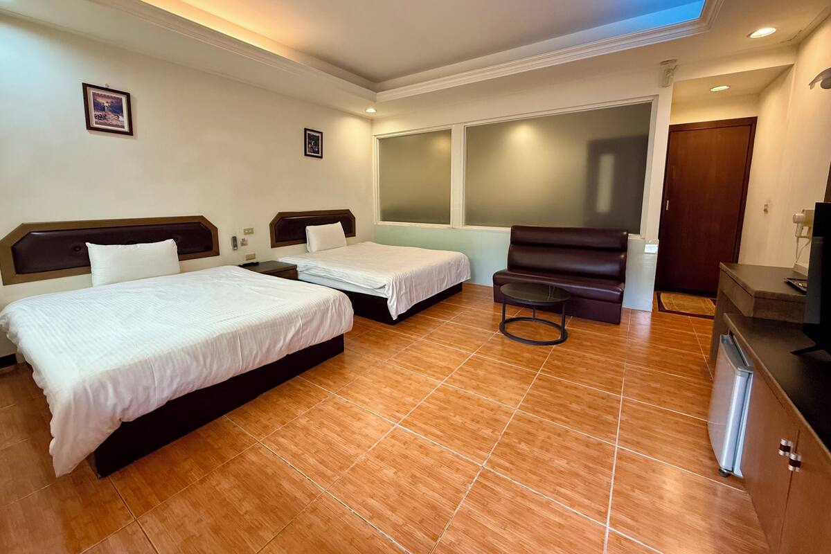 A hotel room with two beds, a small table, a chair, a TV, and a window.