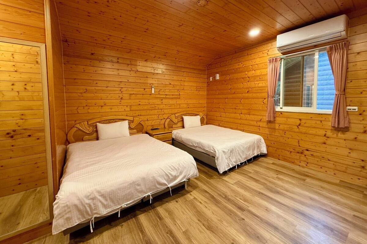 A cabin with two wooden beds, a window with curtains, and an air conditioning unit.