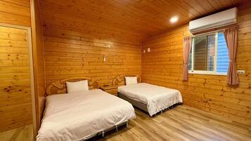 A cabin with two wooden beds, a window with curtains, and an air conditioning unit.