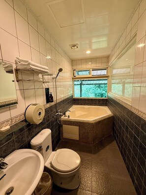 Een badkamer met een bad, toilet, wastafel en een raam met uitzicht op groen.
