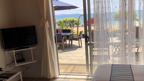 Habitación de hotel con cama, televisión y puerta corrediza de vidrio que da a un área exterior con mesa y sillas.