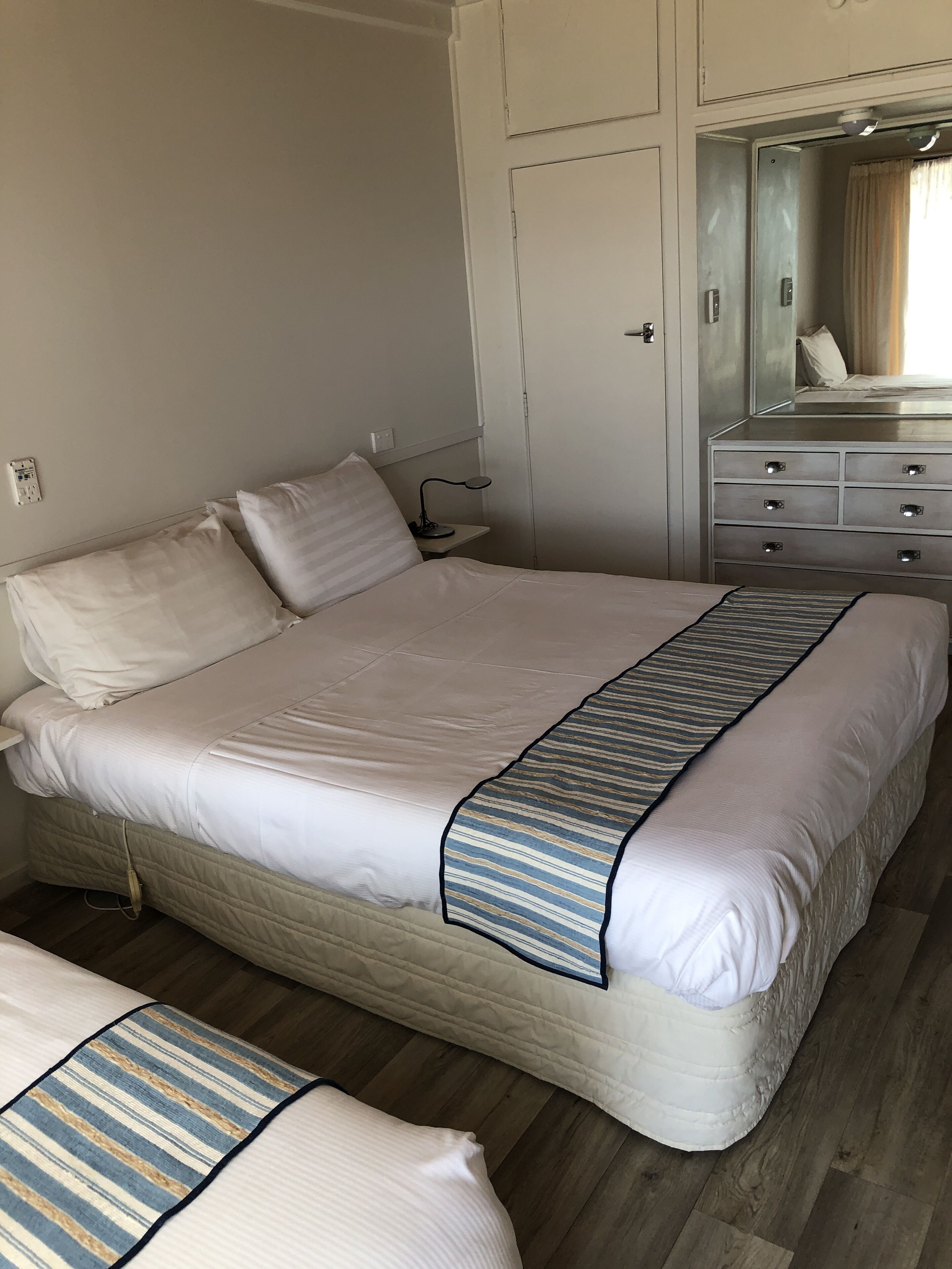A neatly arranged bedroom with a large bed, bedside tables, a dresser, and a mirror.