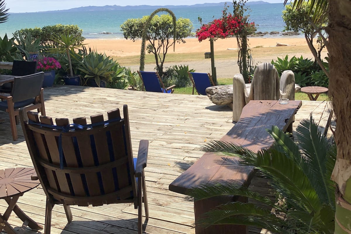 A wooden deck with outdoor furniture, a view of the beach, and tropical plants.