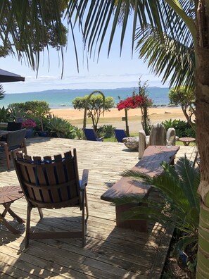 A wooden deck with outdoor furniture, a view of the beach, and tropical plants. - Driftwood Lodge (Cable Bay)