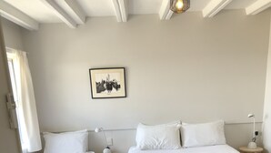 Habitación de hotel con dos camas, una mesita con una silla, una lámpara y un cuadro en la pared.